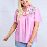 Woman with blonde hair standing in a front profile position wearing the Reece Top against a white background. The focal point of this image is the details on front of top as well as the intricate fabric detail. The model paired this top with a light-wash denim skirt. 