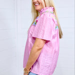 Woman with blonde hair standing in a side profile position wearing the Reece against a white background. The focal point of this image is the pleating down the sleeve as well as the high ruffled collar. The model paired a light-wash denim skirt with this top. 