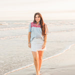 Woman with dark hair standing in a front profile position wearing the Reece Top in a lifestyle scene. The focal point of this image is the tops entirety including patter and fabric. The model paired this top with a white denim skirt. 