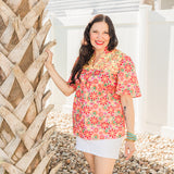 Woman with dark hair is standing in a front profile position wearing the Reece Top in a lifestyle background. The focal point of this image is the top in its entirety as well as the "real time" scenery. The model has paired this top with a white skirt. 