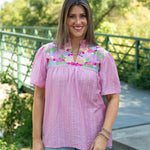 Woman with dark hair standing in a front profile position wearing the Reece in a lifestyle scene. The focal point of this image is the details and pleating on the front of the top as well as the v-neckline. The model paired this top with light-wash denim jeans.