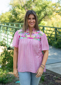 Woman with dark hair standing in a front profile position wearing the Reece in a lifestyle scene. The focal point of this image is the details and pleating on the front of the top as well as the v-neckline. The model paired this top with light-wash denim jeans.