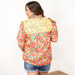 Woman with dark hair standing in a back profile position wearing the Reece Top against a white background. The focal point of this image is the embroidery across the shoulders as well as the graphics along the back of the top. The model has this top paired with dark-wash denim shorts.