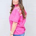 Woman with dark hair standing in a side profile position wearing the Reece Top against a white background. The focal point of this image is the pleating on sleeves and length of top. The model paired this top with dark-wash denim shorts.