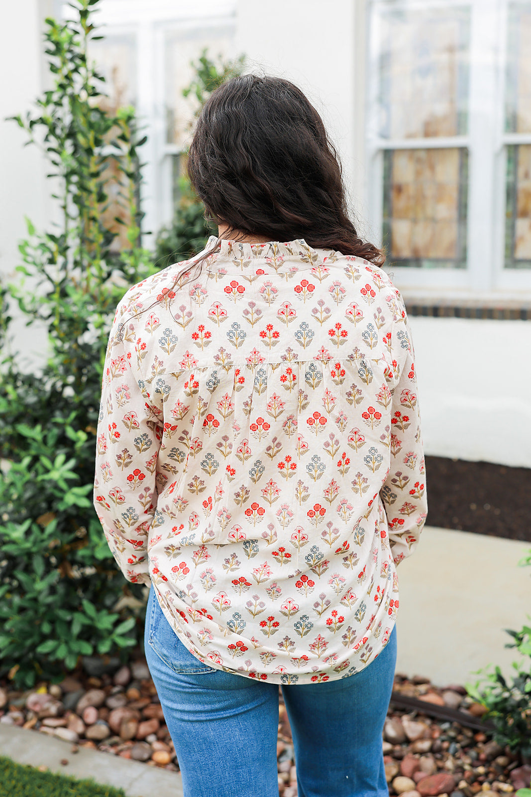 Woman with dark hair wearing a long-sleeve red and blue floral graphic shirt. Model paired this top with dark-wash denim jeans. 
