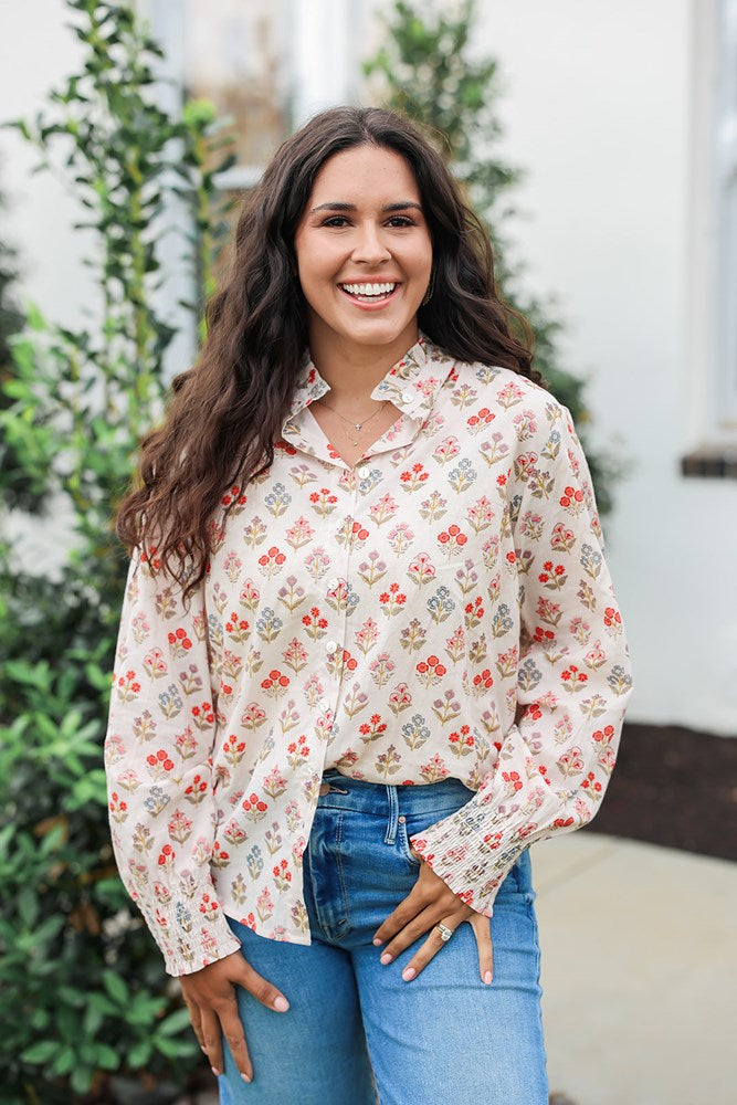 Woman with dark hair wearing a long-sleeve red and blue floral graphic shirt. Model paired this top with dark-wash denim jeans. 