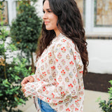 Woman with dark hair wearing a long-sleeve red and blue floral graphic shirt. Model paired this top with dark-wash denim jeans. 