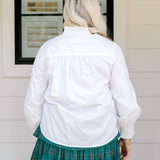 Woman with blonde hair wearing a white long-sleeve top with red ruby buttons down the front. Model paired this top with the Riley Ruffle Skirt. 