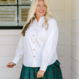 Woman with blonde hair wearing a white long-sleeve top with red ruby buttons down the front. Model paired this top with the Riley Ruffle Skirt. 
