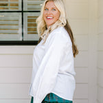 Woman with blonde hair wearing a white long-sleeve top with red ruby buttons down the front. Model paired this top with the Riley Ruffle Skirt. 
