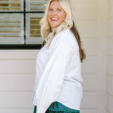 Woman with blonde hair wearing a white long-sleeve top with red ruby buttons down the front. Model paired this top with the Riley Ruffle Skirt. 