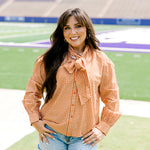 Woman with dark hair wearing a burnt orange gingham long-sleeve top, and light-wash denim shorts. 