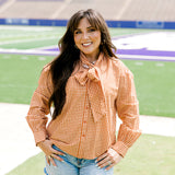 Woman with dark hair wearing a burnt orange gingham long-sleeve top, and light-wash denim shorts. 