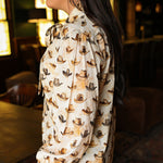 Woman with dark hair wearing a long-sleeve button-down with multi-colored cowboy hats and tying feature in front of top. Model paired this top with light-wash denim jeans. 