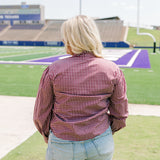 Woman with blonde hair standing in a back profile position wearing the Sadie Top in a lifestyle scene. The focal point of this image is the maroon gingham pattern on back of long-sleeve top. The model paired this top with light-wash denim shorts. 