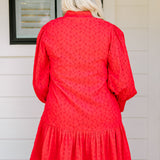 Woman with blonde hair wearing a long-sleeve red eyelet dress with buttons down front, and ruffle at bottom of dress. 