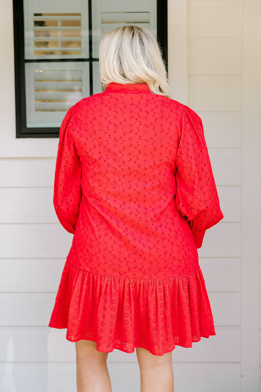 Woman with blonde hair wearing a long-sleeve red eyelet dress with buttons down front, and ruffle at bottom of dress. 
