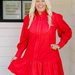 Woman with blonde hair wearing a long-sleeve red eyelet dress with buttons down front, and ruffle at bottom of dress. 