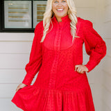 Woman with blonde hair wearing a long-sleeve red eyelet dress with buttons down front, and ruffle at bottom of dress. 