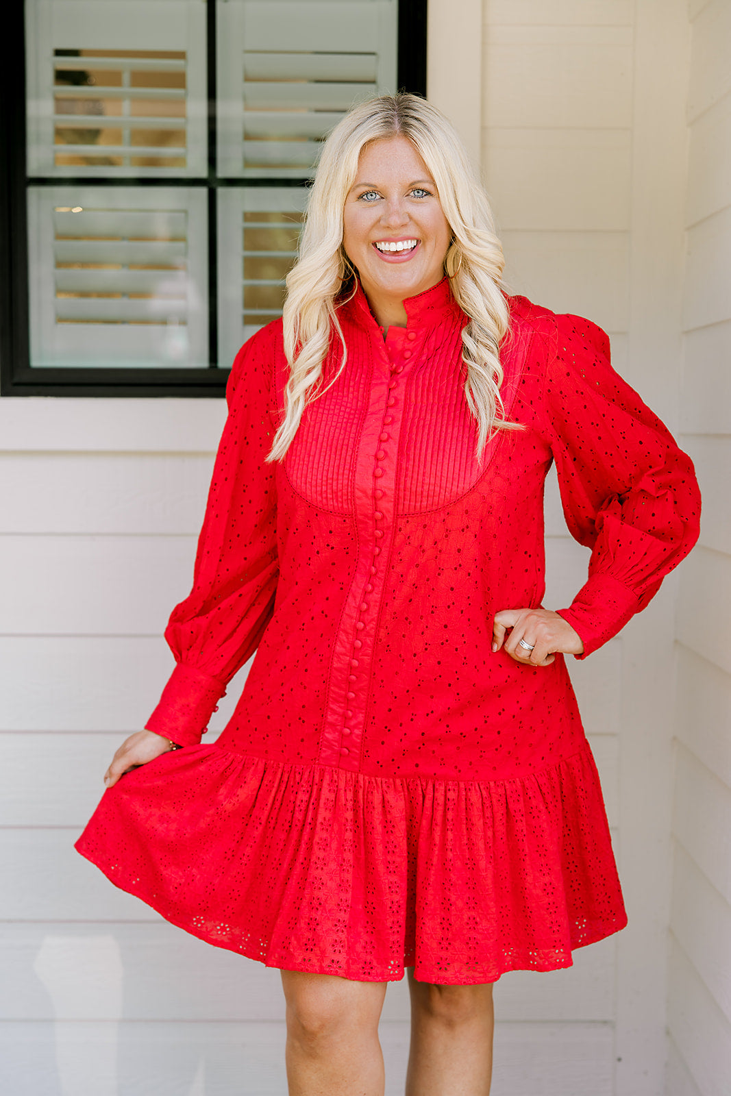 Woman with blonde hair wearing a long-sleeve red eyelet dress with buttons down front, and ruffle at bottom of dress. 
