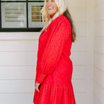 Woman with blonde hair wearing a long-sleeve red eyelet dress with buttons down front, and ruffle at bottom of dress. 