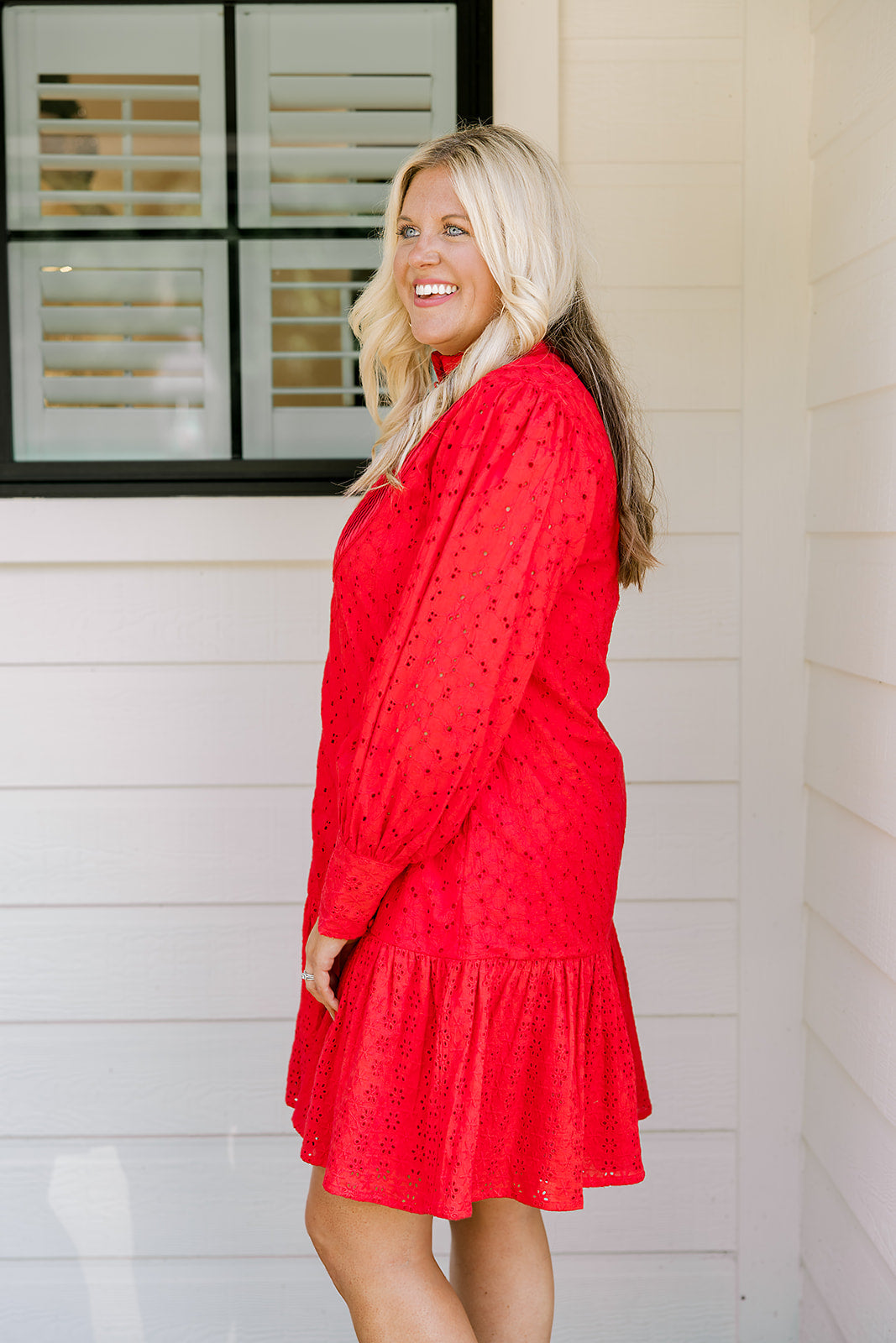 Woman with blonde hair wearing a long-sleeve red eyelet dress with buttons down front, and ruffle at bottom of dress. 