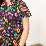 Woman with dark hair in a front facing position with a deep focal length on the front of top. The focal point of this image is the graphics on the front of the top with slight emphasis on the sleeves and ruffled collar.
