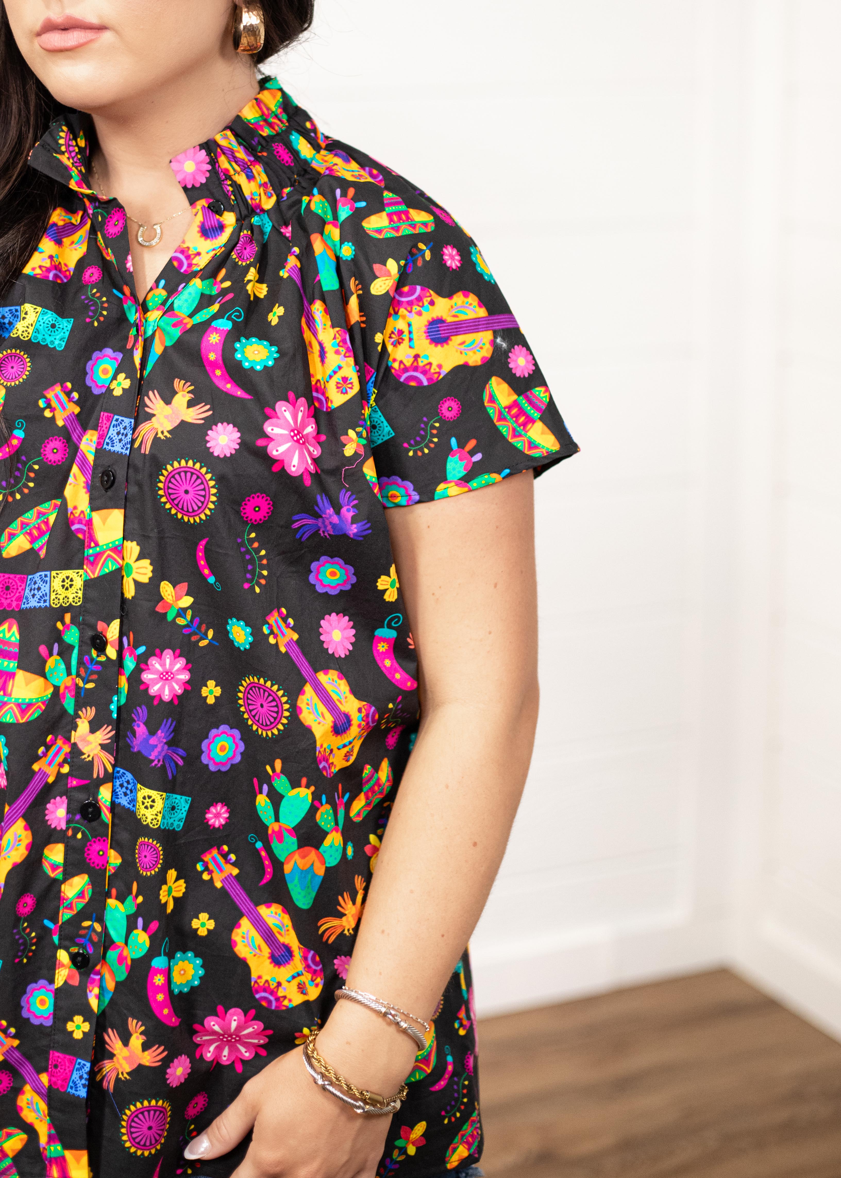 Woman with dark hair in a front facing position with a deep focal length on the front of top. The focal point of this image is the graphics on the front of the top with slight emphasis on the sleeves and ruffled collar.