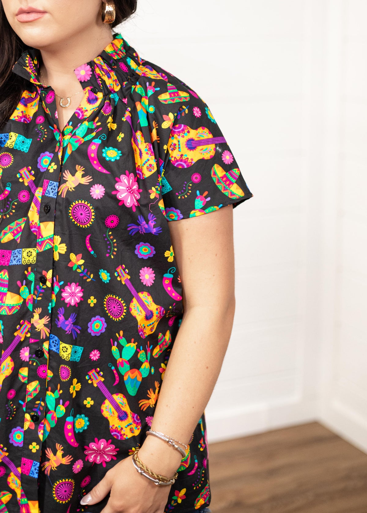 Woman with dark hair in a front facing position with a deep focal length on the front of top. The focal point of this image is the graphics on the front of the top with slight emphasis on the sleeves and ruffled collar.