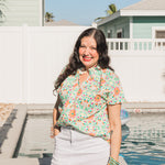 Woman with dark hair standing in a front profile position wearing the Sarah Top in a lifestyle scene. The focal point of this image is to the see the top in its entirety as well as give it a "real time" look. Model is wearing a white denim skirt to pair with top.