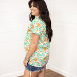 Woman with dark hair standing in a side profile position wearing the Sarah Top against a white background. The focal point of this image is the side graphics of the top as well as seeing length of top and sleeves. The model paired this top with dark-wash denim shorts.