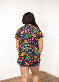 Woman with dark hair wearing the Sarah Top standing in a back profile position against a white background. The focal point of the image is the graphic design on the back of the top. Model paired top with dark-wash denim jeans. 
