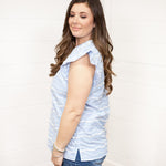 Woman with dark hair standing in a side profile position wearing the Scarlett Top against a white background. The focal point of the top is the ruffled sleeve and embroidery detail on top. The model paired this top with dark-wash denim shorts