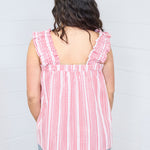 Woman with dark hair standing in a back profile position wearing the Sophia Top against a white background. The focal point for this image is the ruffled straps and gingham graphics. The model paired this top with light-wash denim jeans. 
