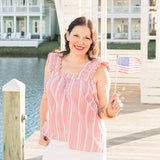 Woman with dark hair standing in a front profile position wearing the Sophia Top in a lifestyle scene. The focal point in this image is the entirety of the top. The model paired this top with a white skirt. 