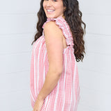 Woman with dark hair standing in a side profile position wearing the Sophia Top against a white background. The focal point for this image is the sleeve ruffles, gingham graphic, and length of top. The model paired this top with light-wash denim jeans.