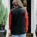 Woman with dark hair wearing long-sleeve top with embroidered cowboy Santa on front and red sparkle sleeves. Model paired this top with light-wash denim jeans. 