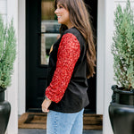 Woman with dark hair wearing long-sleeve top with embroidered cowboy Santa on front and red sparkle sleeves. Model paired this top with light-wash denim jeans. 
