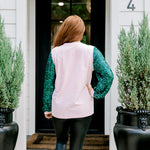 Woman with red hair wearing a sweater with green sparkle sleeves, and multi-color tree embroidery on front with words "Merry & Bright" on front. Model paired this top with faux leather leggings. 