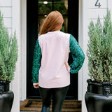 Woman with red hair wearing a sweater with green sparkle sleeves, and multi-color tree embroidery on front with words "Merry & Bright" on front. Model paired this top with faux leather leggings. 