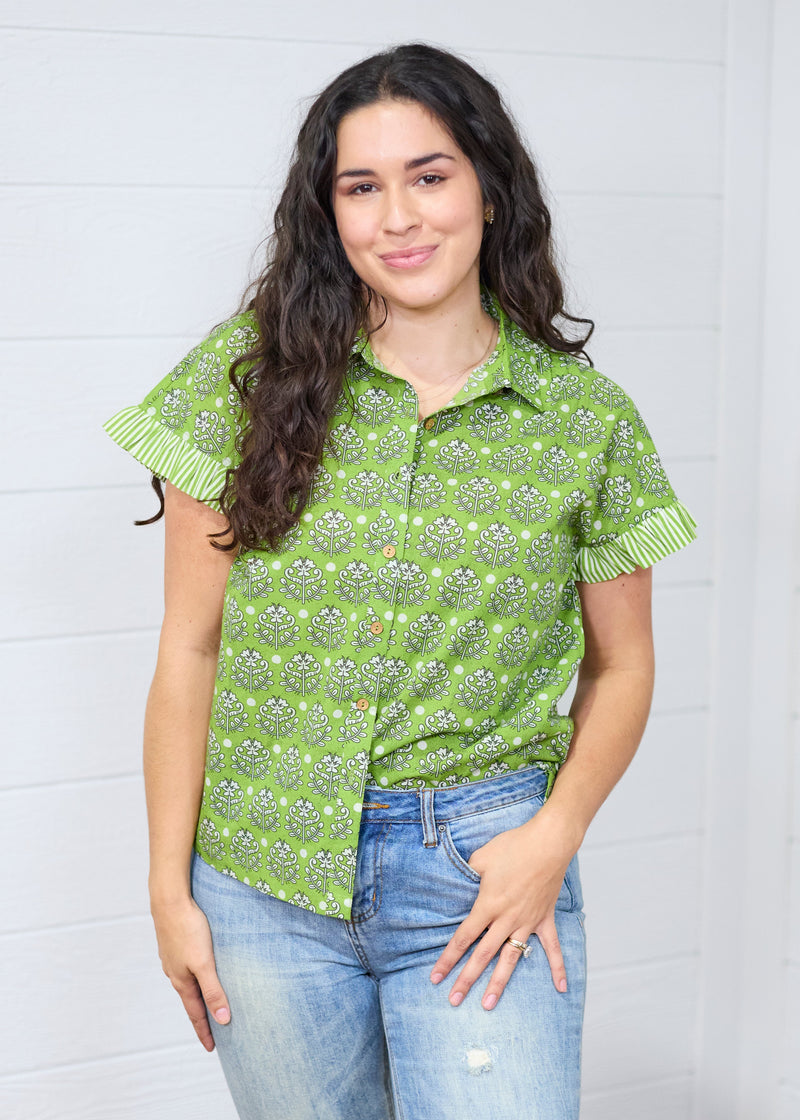 Woman with dark hair standing in a front profile position wearing the Stevie Top against a white background. The focal point of this image is the buttons down the front of the top as well as graphics and collared neckline. The model paired this top with light-wash denim jeans.