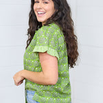 Woman with dark hair standing in a side profile position wearing the Stevie Top against a white background. The focal point of this image is the graphics on the side of the top along with a better view of the striping on the cuff. The model paired this top with light-wash jeans. 