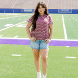 Woman with dark hair standing in a front profile position wearing the Stevie Top in a lifestyle scene. The focal point of this image is the flower graphics on the front of top as well as the wooden buttons down the front. The model paired this top with light-wash denim shorts.