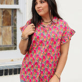 Woman with dark hair standing in a front profile position wearing the Stevie Top against a white background. The focal point of this image is the pink and orange floral, buttons down the front, as well as the low collar and ruffled sleeves. The model paired this top with dark-wash denim jeans. 