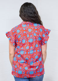 Woman with dark hair standing in a back profile position wearing the Stevie Top against a white background. The focal point for this image is the pleated back and graphics. The model paired this top with dark-wash denim jeans. 
