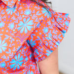 Woman with dark hair standing in a front profile position wearing the Stevie Top against a white background. The focal point of this image is the deep focus on the ruffled shoulder and graphics on shirt. 
