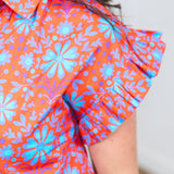 Woman with dark hair standing in a front profile position wearing the Stevie Top against a white background. The focal point of this image is the deep focus on the ruffled shoulder and graphics on shirt. 