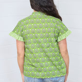 Women with dark hair standing in a back profile position wearing the Stevie Top against a white background. The focal point of this image is the graphics on the back of the top and striping along the cuff. The model paired this top with light-wash denim jeans.