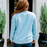 Woman with red hair wearing a baby blue sweatshirt with Christmas motif embroidery. Model paired this top with dark-wash denim jeans. 