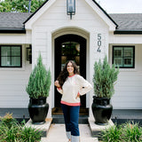 Woman with dark hair wearing a sweatshirt with red & white striping along cuff and collar. On the back of top there is a multi color bible verse. Model paired this top with dark-wash denim jeans. 